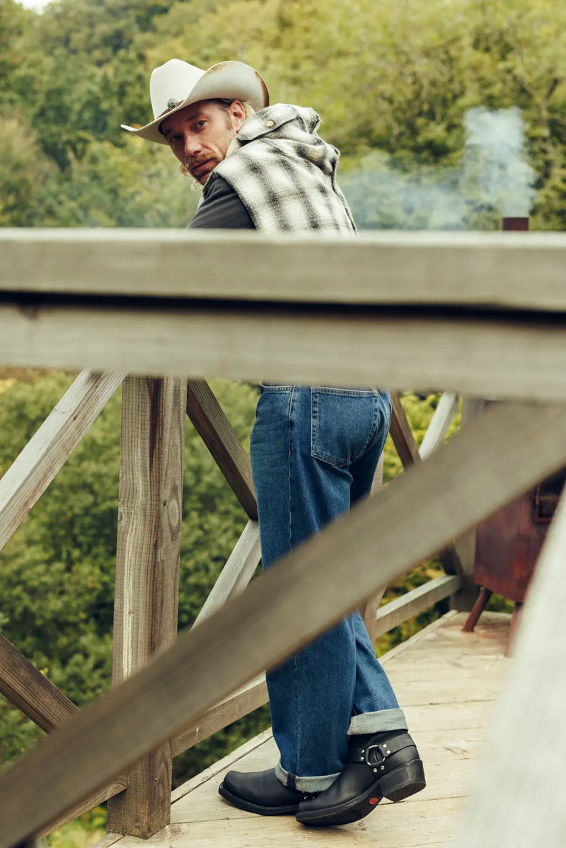 A man stood on a wooden balcony, wearing a trilby hat and a pair of Durango Western Boots